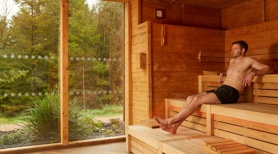 Man lounging in a Nordic Sauna looking out to the forest