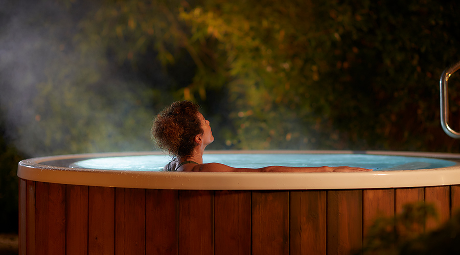 Woman soaking in a hot tub surrounded by the forest.