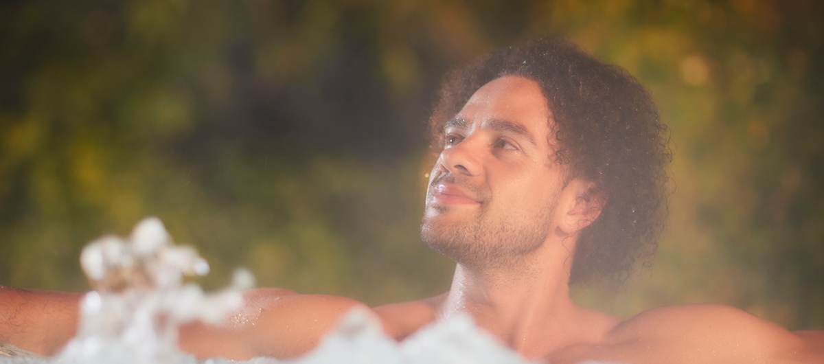 Man soaking in an outdoor hot tub surrounded by the forest.