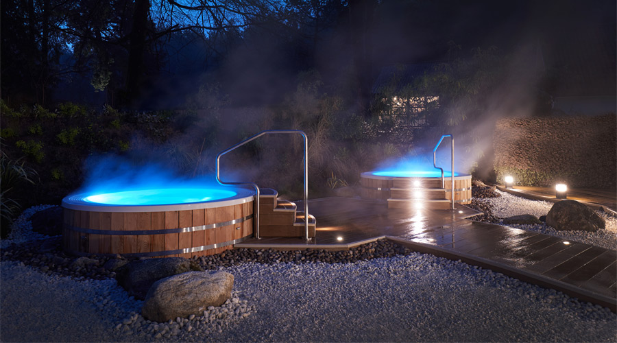 Two steaming outdoor hot tubs at night, both with steps leading up.