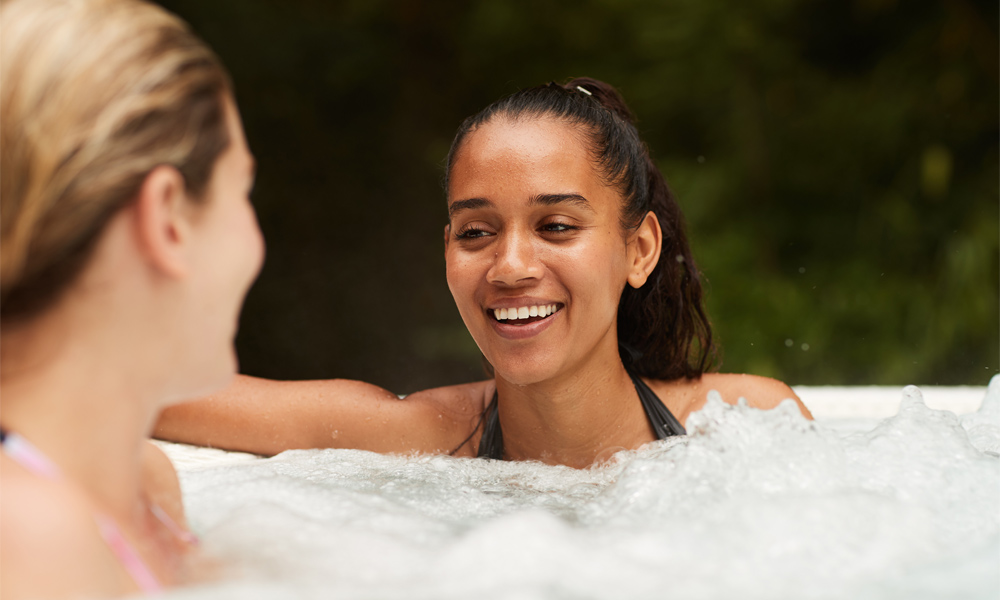Two women soaking in an outdoor hot tub surrounded by the forest.