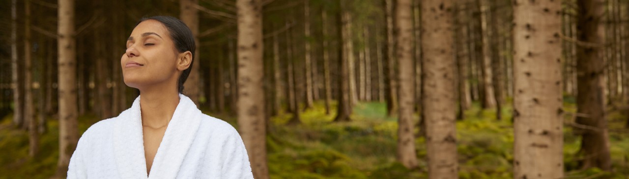 Woman with her eyes closed breathing in the surrounding forest.