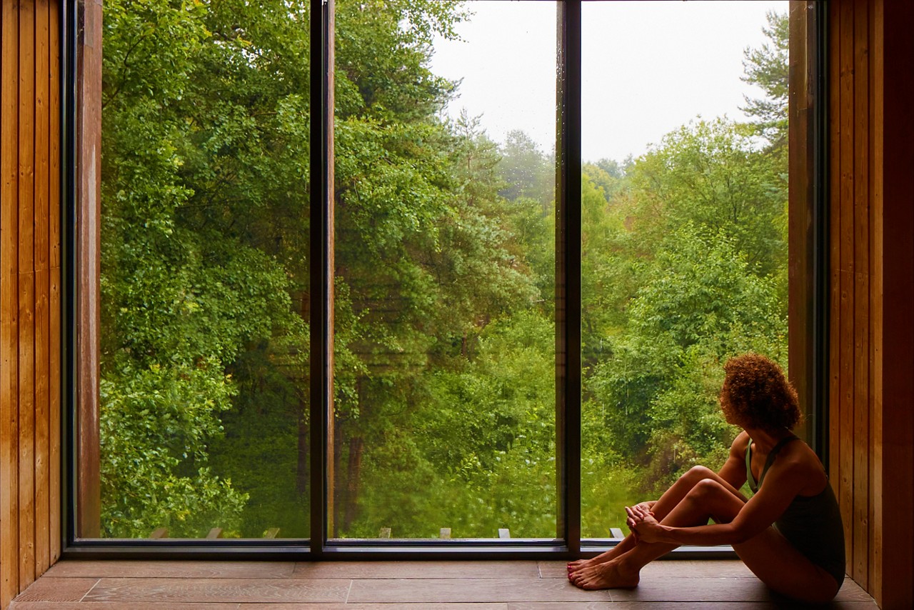 Woman sat looking out at the forest from inside the Treetop Sauna.