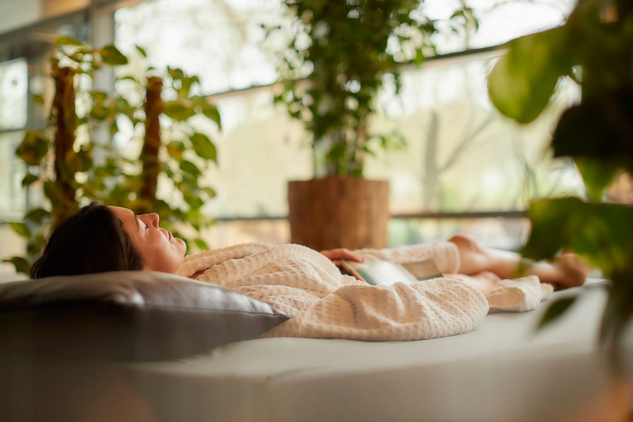 Woman laid on a Waterbed in a serene area with lots of plants and natural light.
