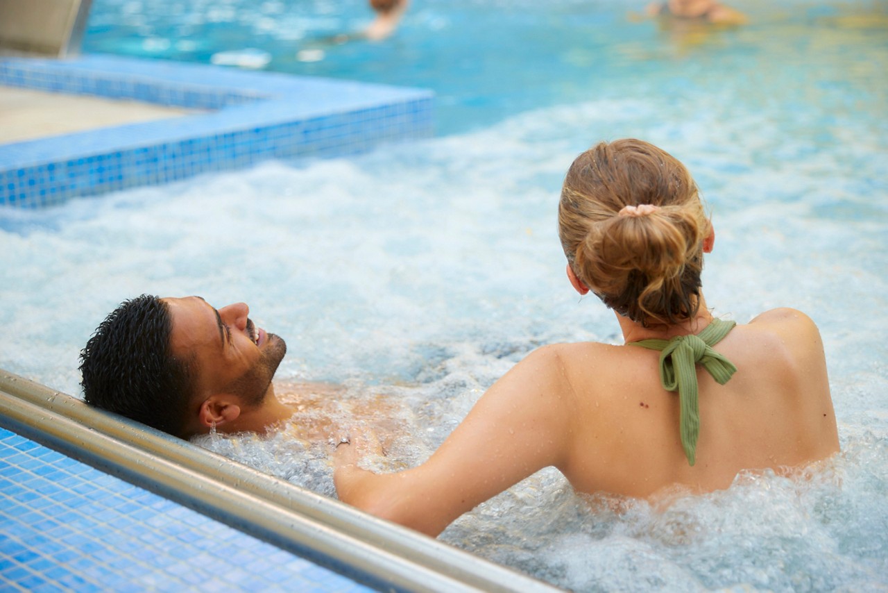 two people in an outdoor pool leaning on the side 