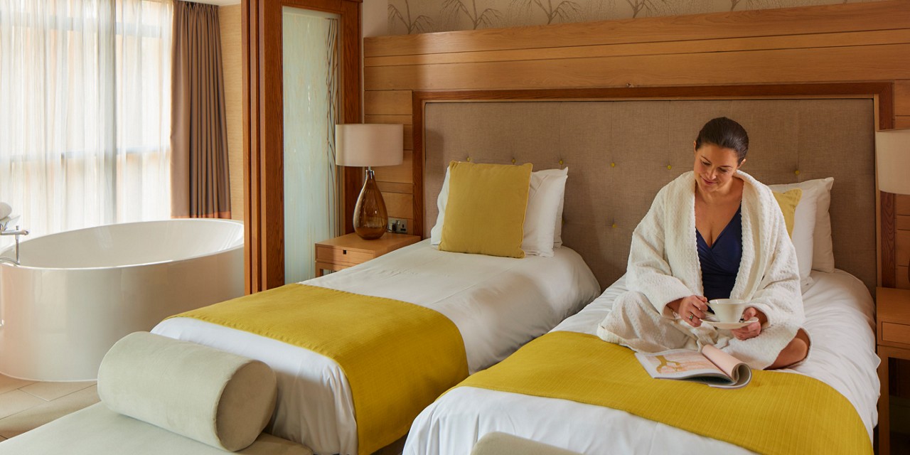 Woman sitting on a twin bed in a Spa Suite reading a book.