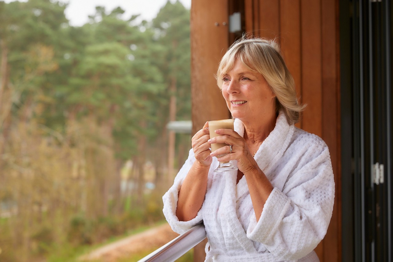 Woman drinking a coffee whilst looking out to the forest