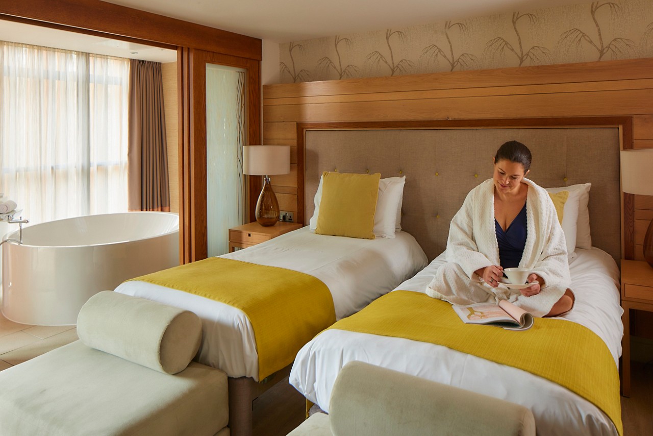 Woman sitting on a twin bed in a Spa Suite reading a book.