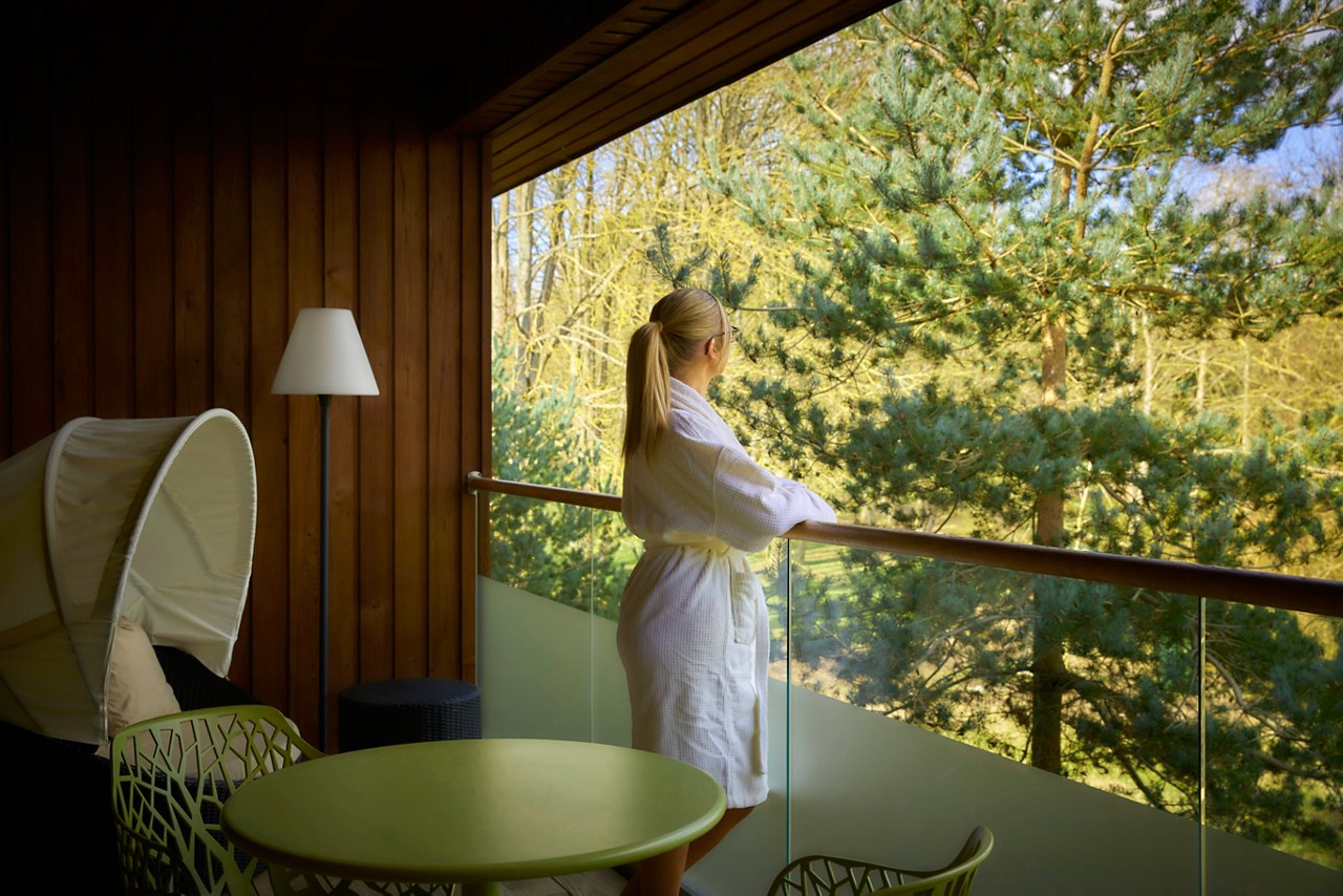 women in a spa robe standing on suite balcony looking at forest view
