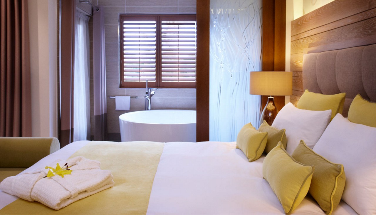 Double bed with a neatly folded spa robe and a large bathtub.