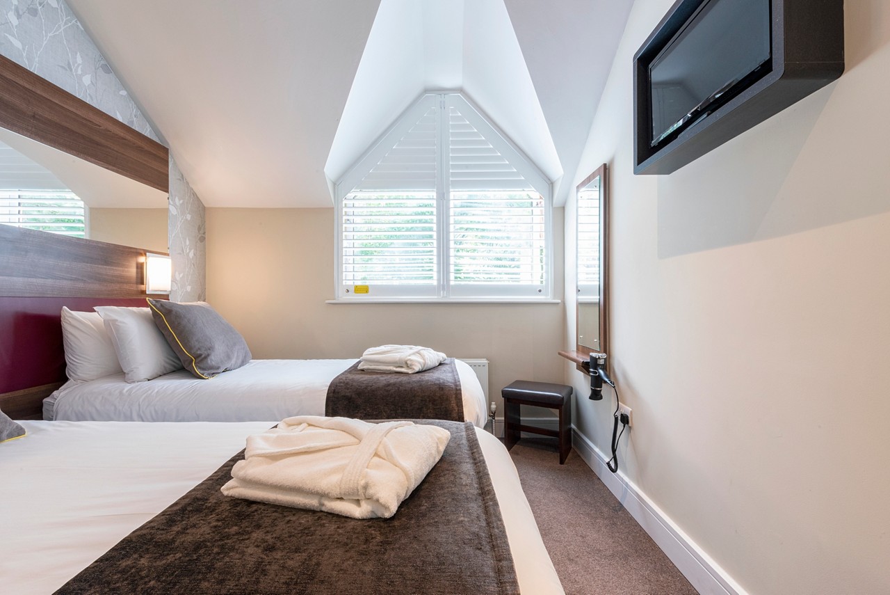 a twin bedroom in Sherwood Forest Spa Suites Apartment, featuring two twin beds made up with white linens, grey pillows and folded white robes on top