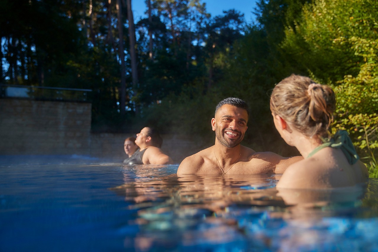 People in an outdoor swimming pool smiling with forest trees in the background