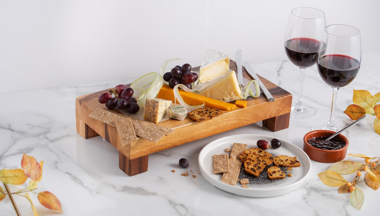 Wooden tray with cheese and grapes with two glasses of red wine next to it 
