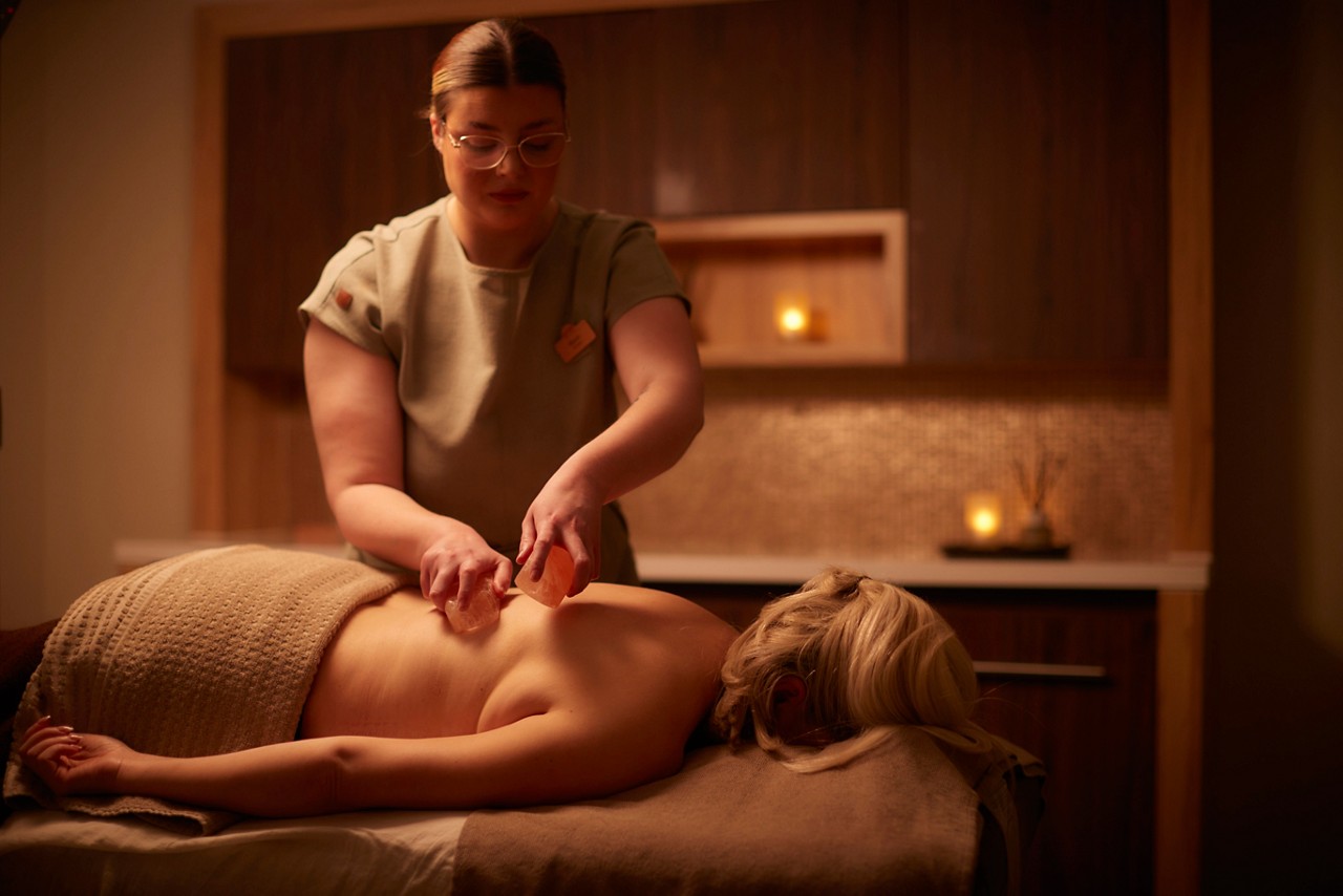 A massage therapist performing a comfort zone Himalayan salt ritual on a clients back