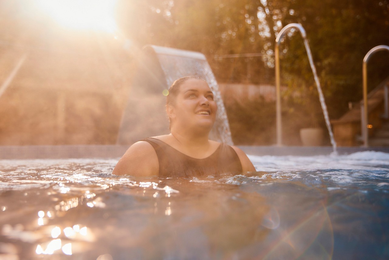 Women un a black swimsuit in a an outdoor pool surrounded by forest
