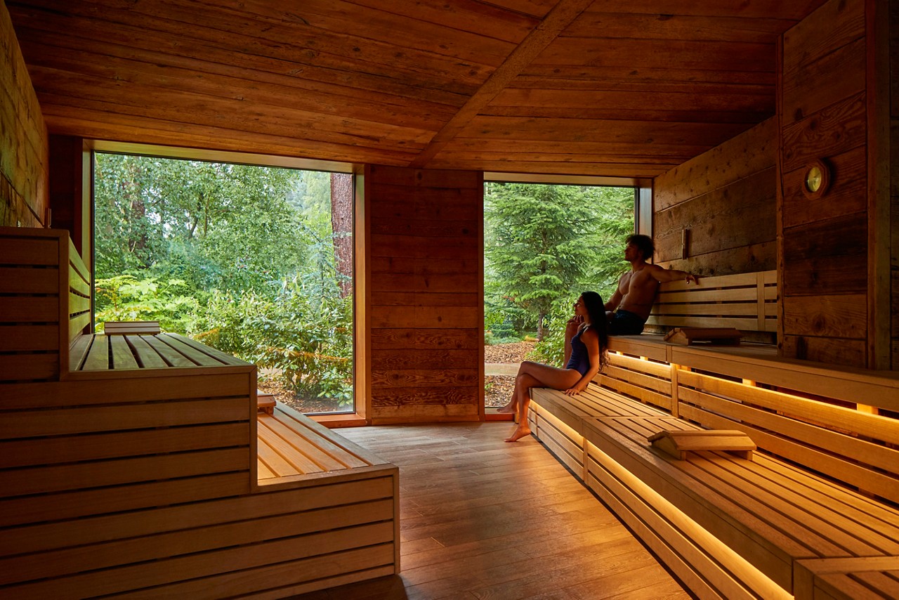 Man and woman sitting enjoying the forest views from inside the Nordic Sauna.