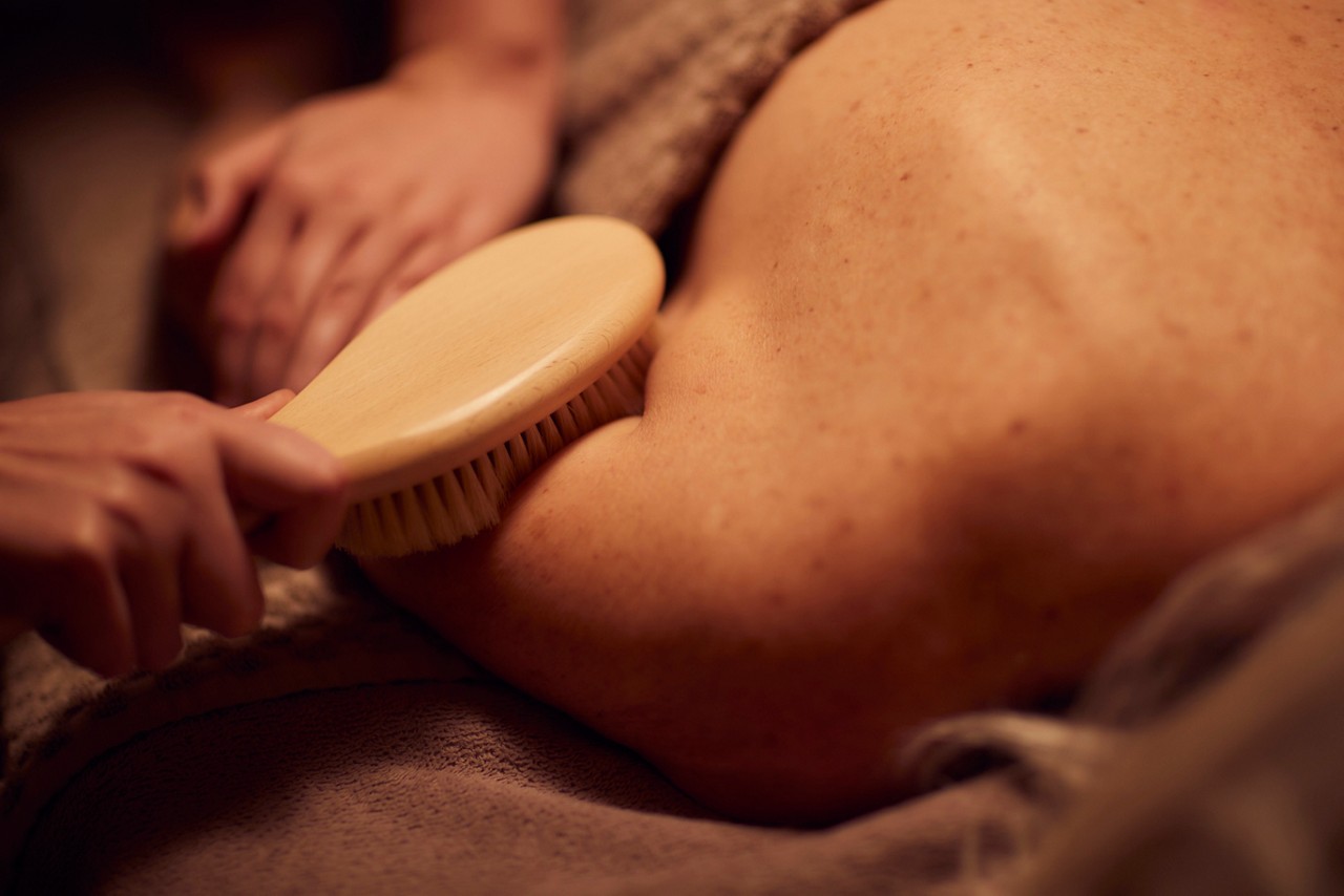 Spa therapist giving a woman a body brush treatment.