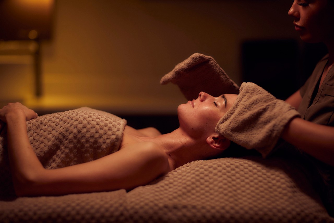 A spa therapist giving a facial treatment to client lying on a spa bed