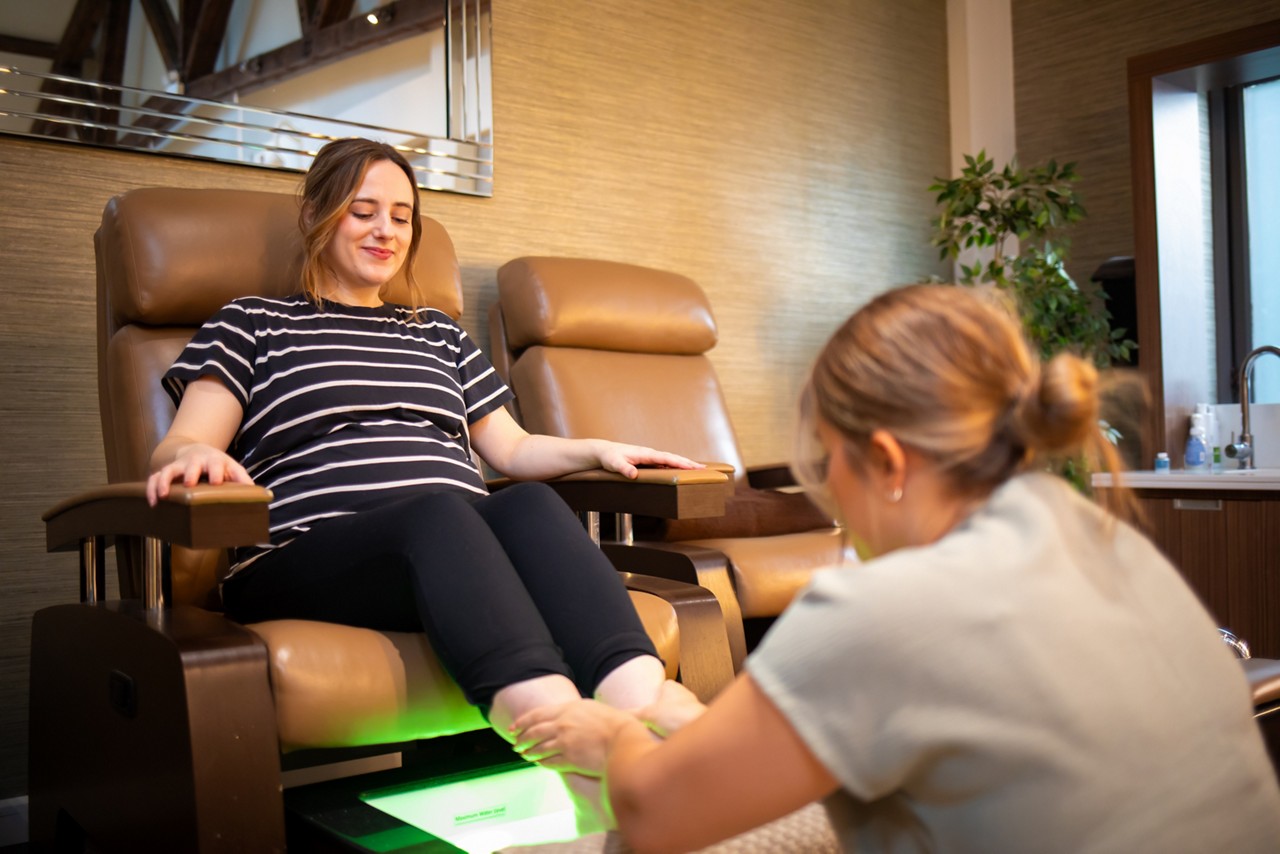 women in blue and white top sat in a relaxing chair getting a pedicure
