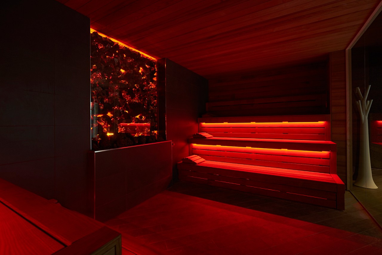 inside the Lava sauna at Aqua Sana, featuring rows of warm lit wooden seating on both sides and glowing feature wall on one side