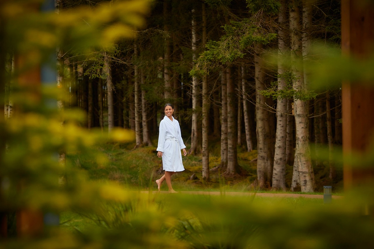 Lady dressed in a soft spa robe as she walks bare foot along a forest path.