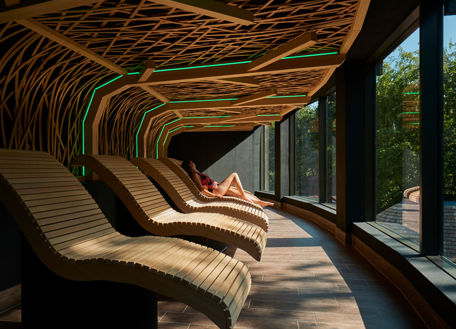Woman relaxing in a wooden sauna with panoramic views of the forest.