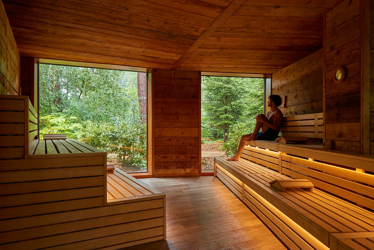 Man sitting inside a wooden Nordic Sauna with forest views.
