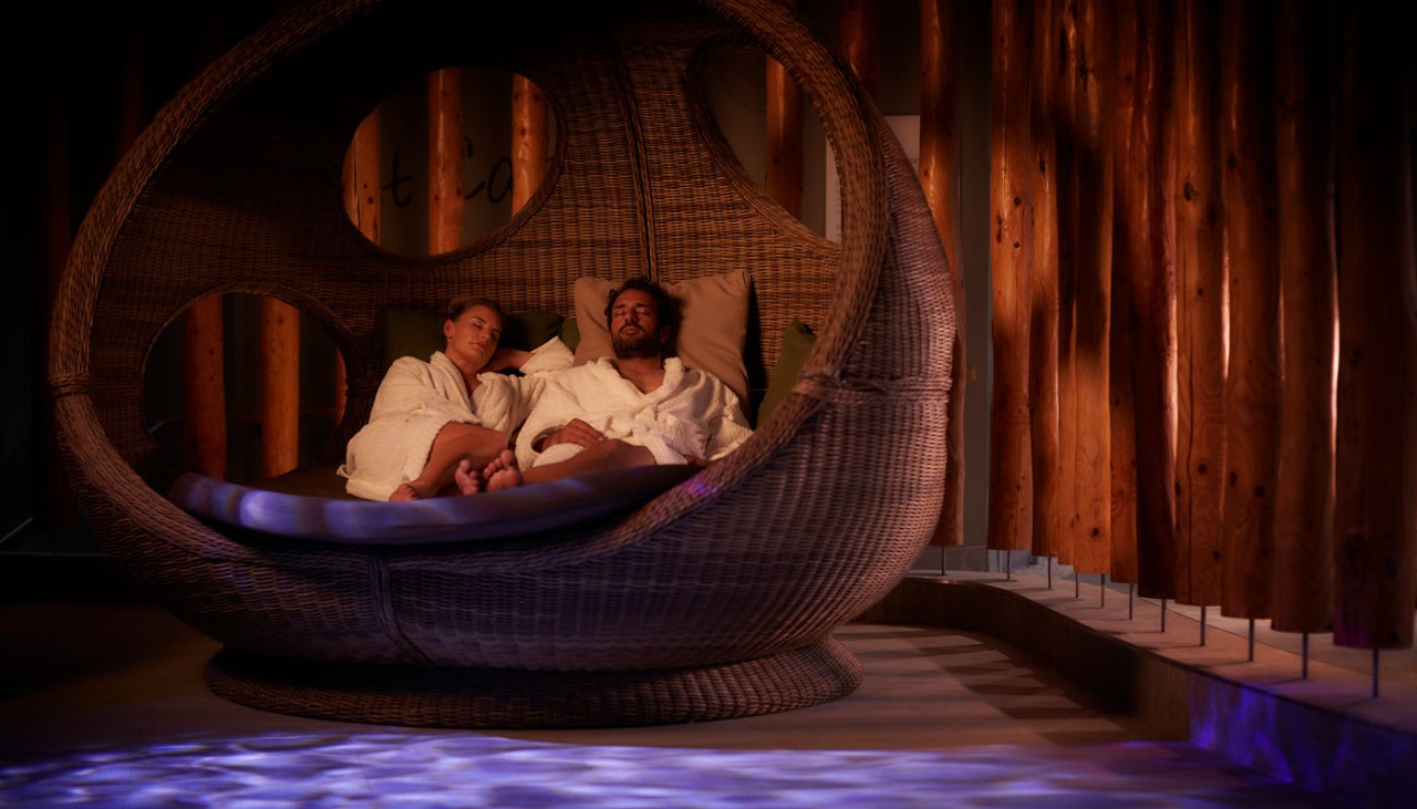 Couple snuggled in a large, cosy cocoon chair.