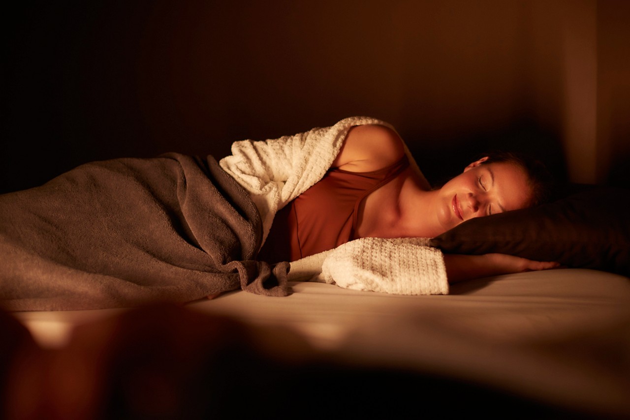A person lying comfortably on a bed with a pillow, experiencing a deep relax treatment in a dimly lit cozy room