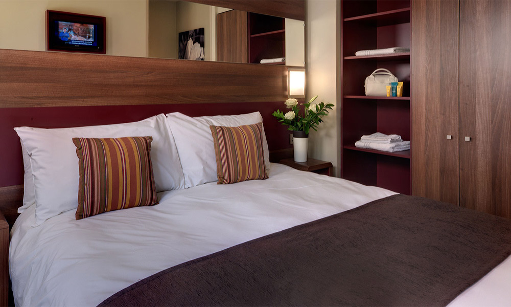 Comfortable bed with vase of flowers beside.