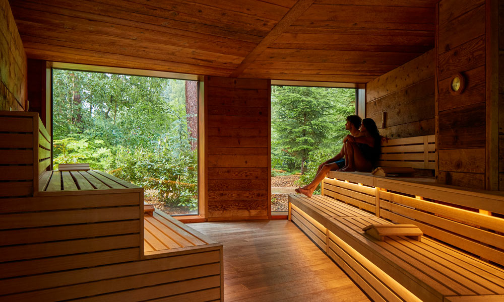 Couple sitting in the Nordic Sauna enjoying views of the forest.