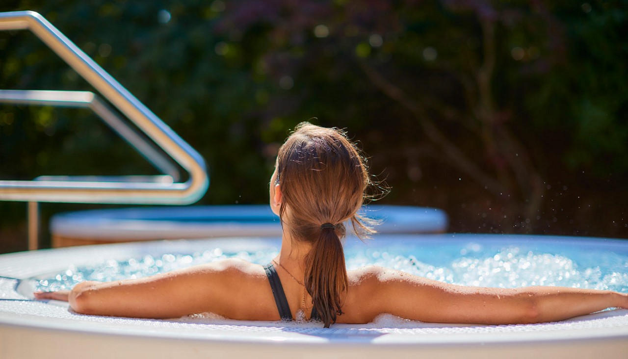 Woman looking out to the forest sitting in a bubbling hot tub.