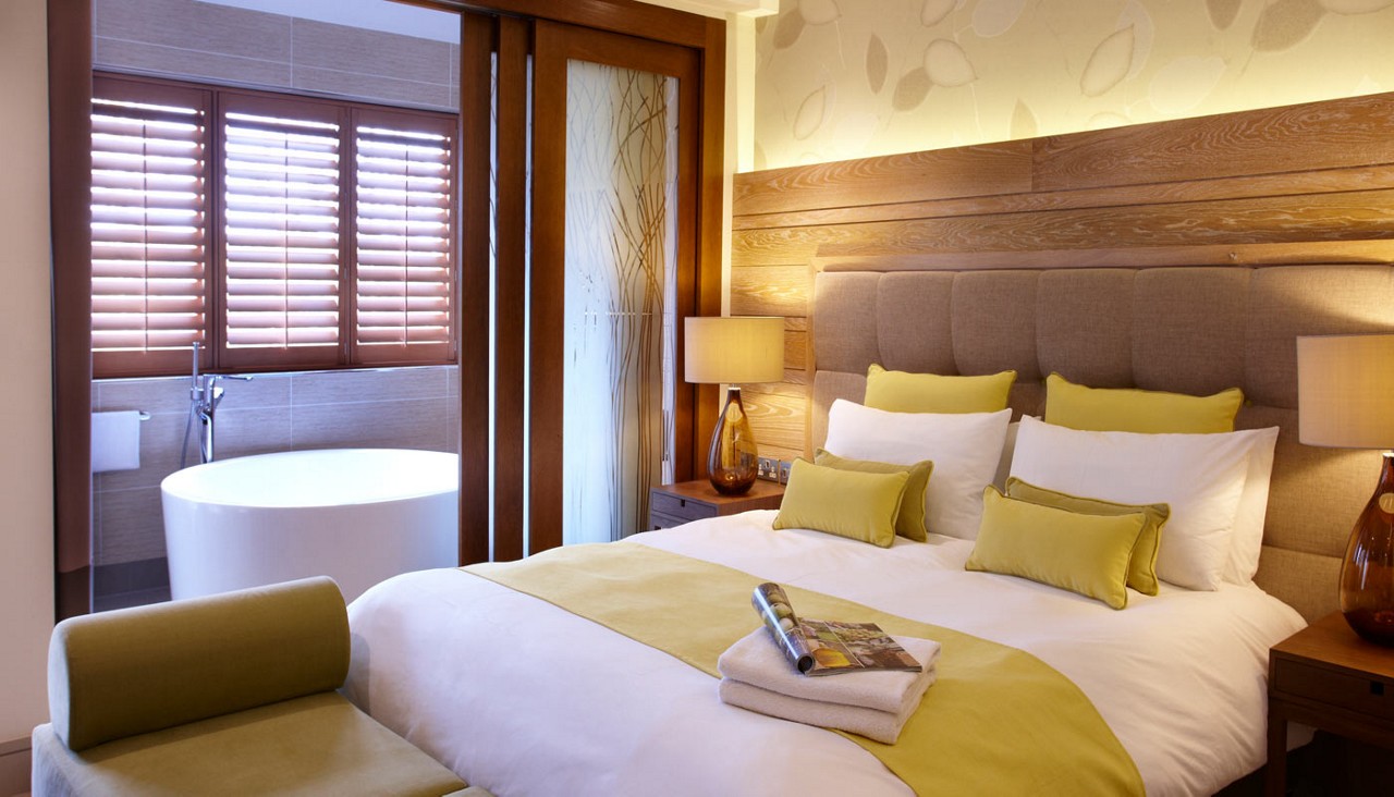 Double bed with neatly folded towels and a large bathtub.