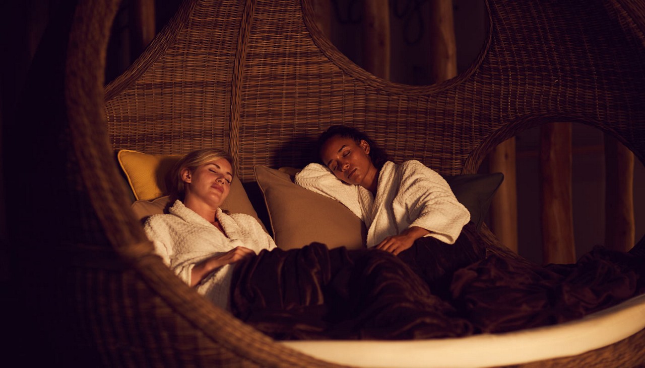 Two ladies sleeping in a cosy cocoon seat.