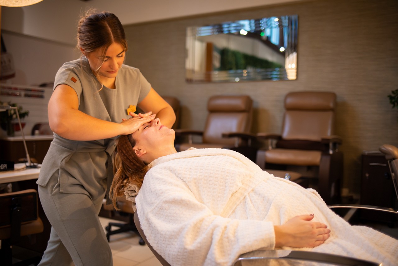 A therapist giving a facial treatment to a pregnant client reclining in a spa chair