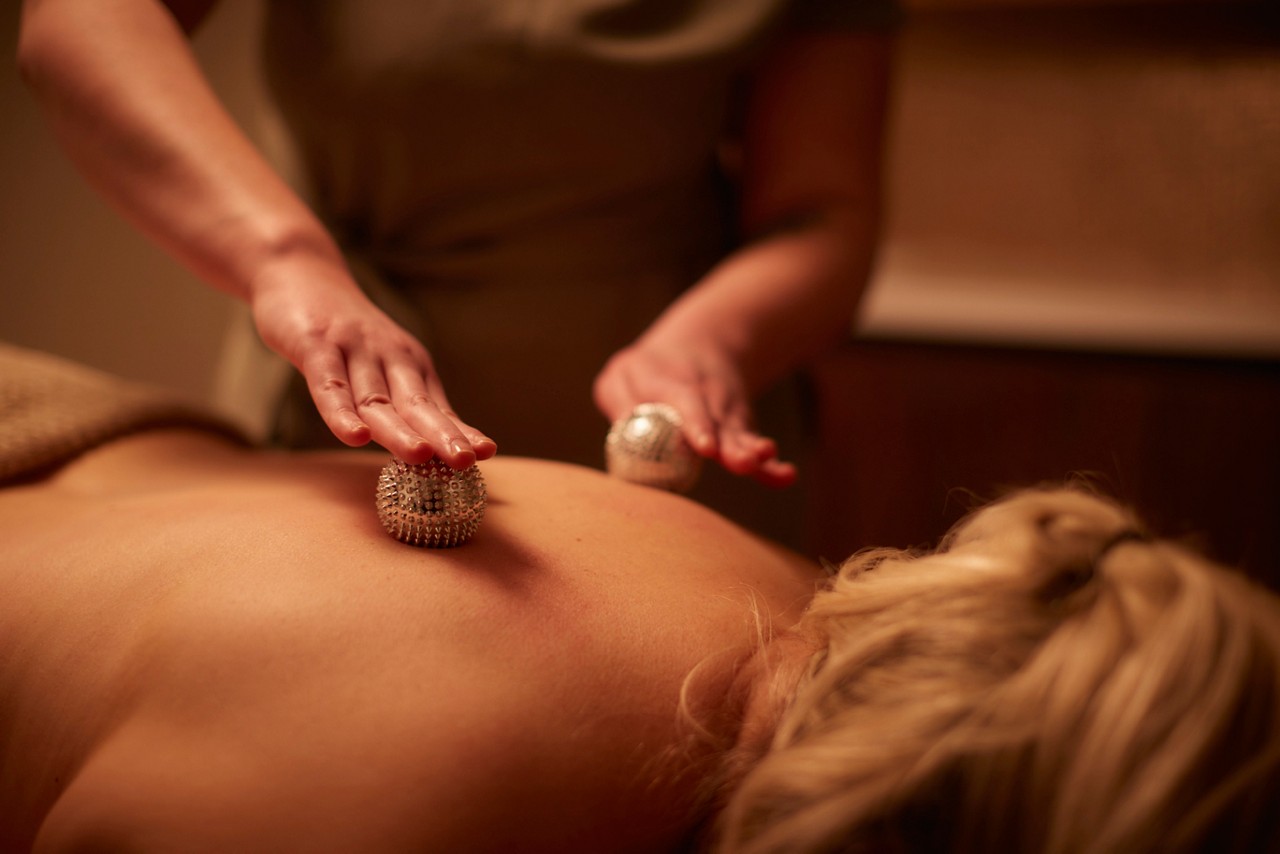 A massage therapist giving a client a massage on their back using two cryo spheres